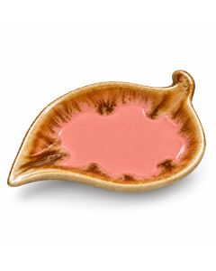 Roze keramieken bladschaaltje met een gebruikt theezakje op een rustieke houten tafel, naast een dampende kop thee, een linnen doek en witte bloemen.